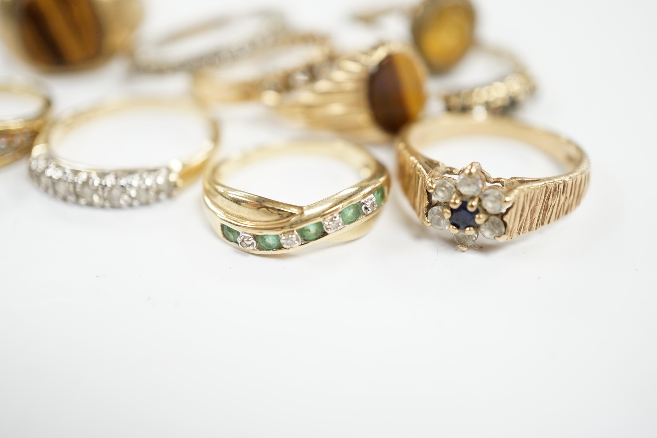 Ten assorted modern 9ct gold and mainly gem set rings, including two with tiger's eye quartz and a seven stone half hoop diamond set, size M/N, gross weight 25.5 grams. Condition - fair